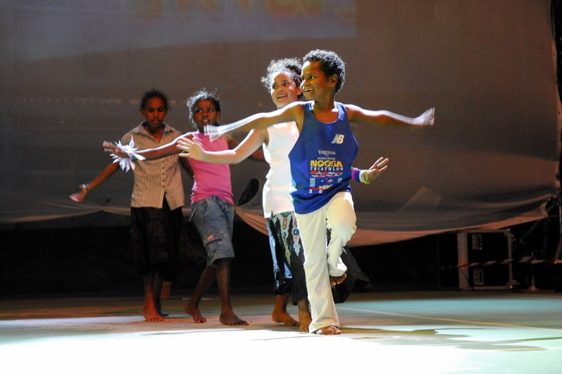 Boy dancing with his arms out and other kids in line behind him.