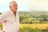 A man looking worried with a bushfire burning in the background