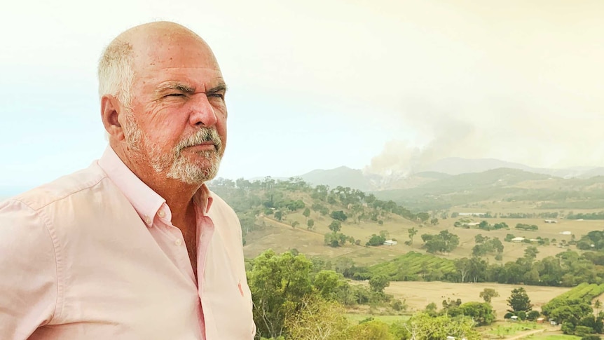 A man looking worried with a bushfire burning in the background