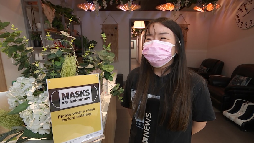 A woman in a black shirt and pink masks stands next to a sign indicating masks need to be worn in the venue
