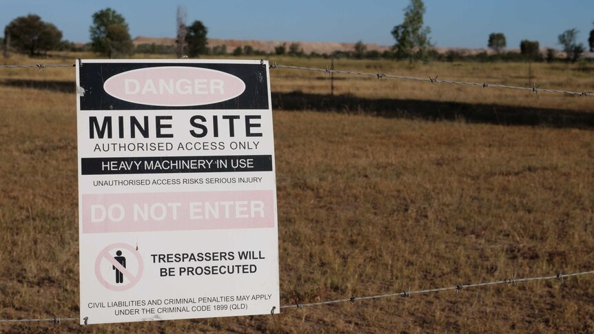 a sign saying "do not enter" is stuck to a barbed wire fence, with a mine in the background