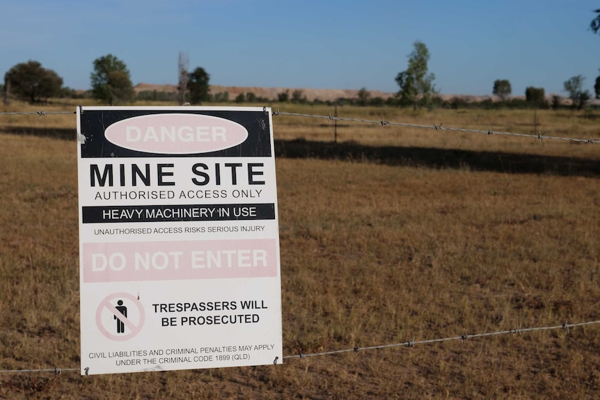a sign saying "do not enter" is stuck to a barbed wire fence, with a mine in the background
