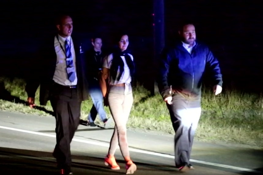 Two men and a woman walking along a road at night.