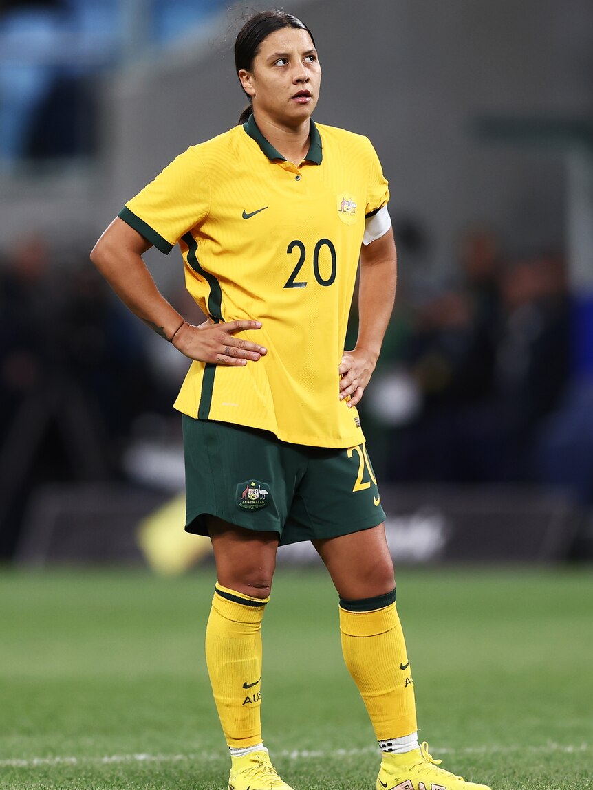A woman soccer player wearing yellow and green puts her hands on her hips