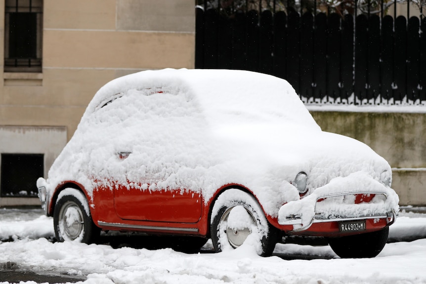 A snow-covered fiat 500 is parked in a Paris street.
