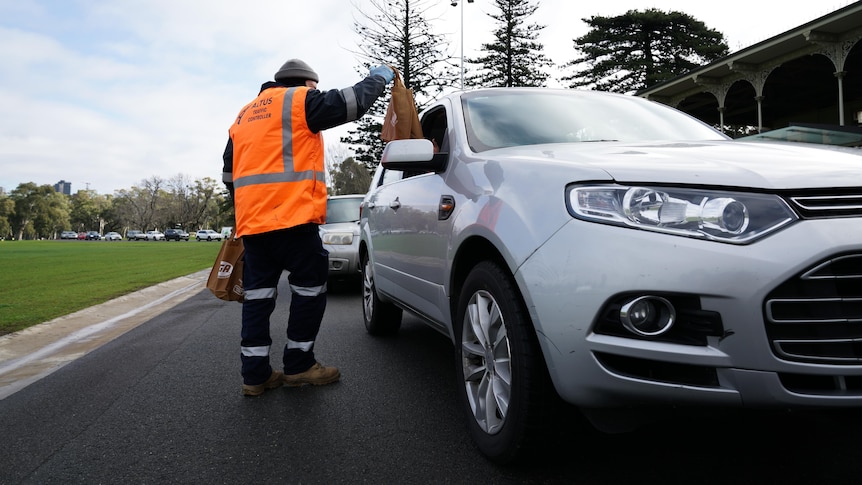 A person in an orange vest hands food in a bag to people inside a car