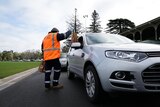 A person in an orange vest hands food in a bag to people inside a car