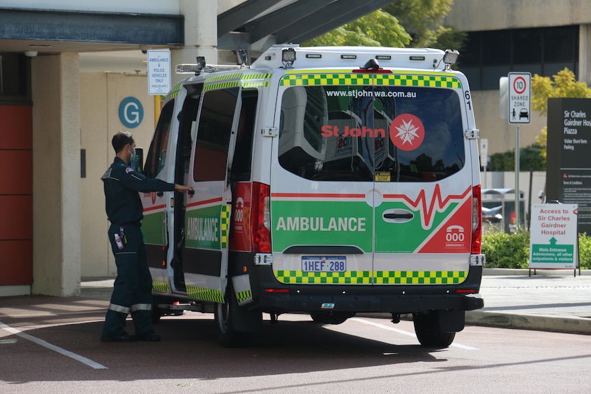 An ambulance parked outside a hospital with a paramedic opening the sliding door on the side of the vehicle.