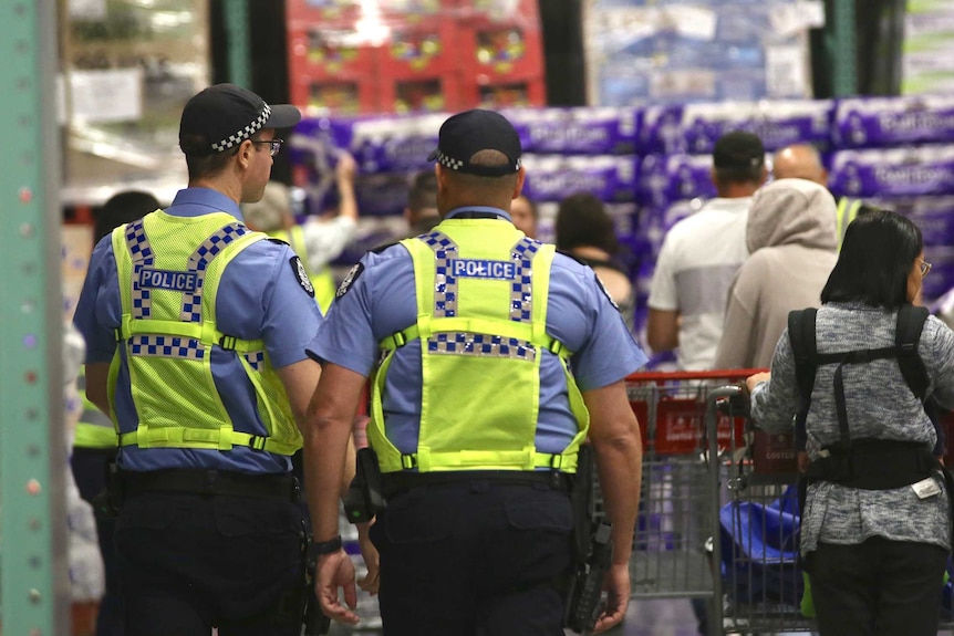 Two police officers with yellow high-viz vests walk through a supermarket surrounded by shoppers.