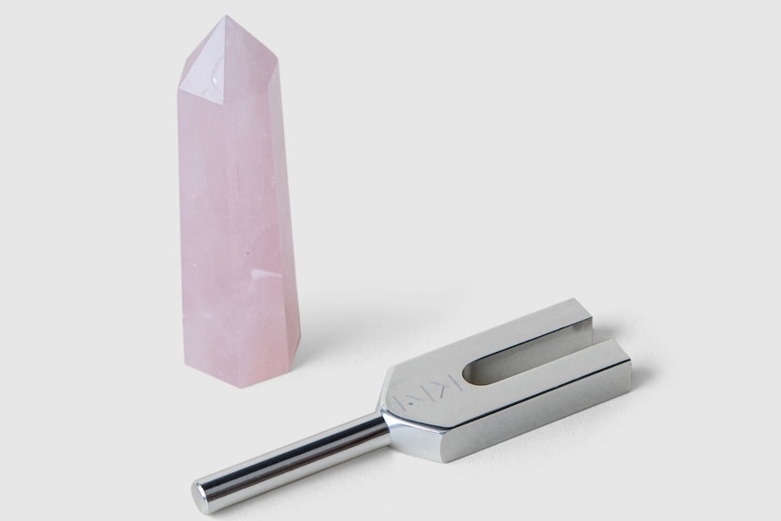 An aluminium tuning fork lies next to a rose quartz crystal.