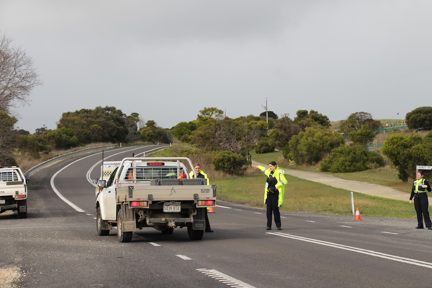 Three police officers stand on a country road, one has her arm extended out to tell the driver of a ute to go that direction