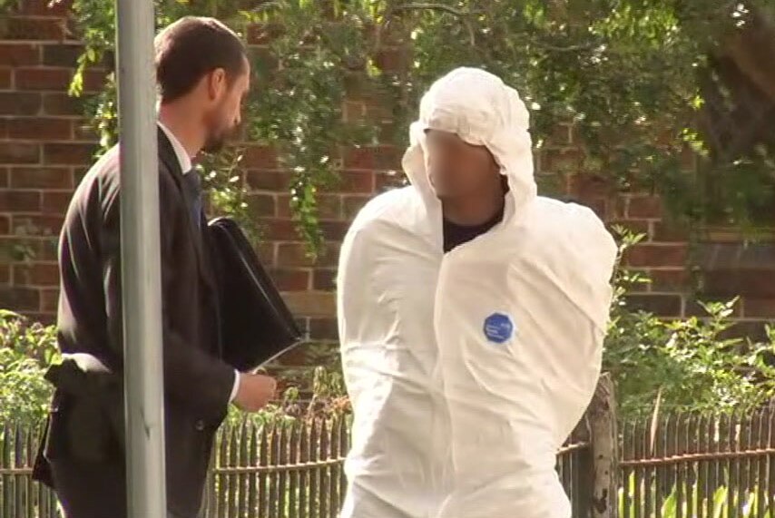 A man, wearing a wife hooded suit, with his face pixelated with a police officer.