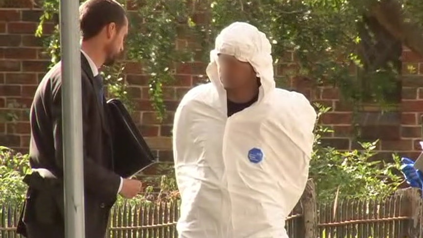 A man, wearing a wife hooded suit, with his face pixelated with a police officer.