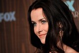 a close up of a smiling Annie Wersching, with dark brown hair and a bronze glittery earring