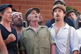 A group of men, wearing hats, singing outdoors