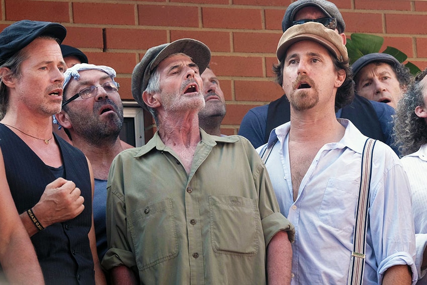 A group of men, wearing hats, singing outdoors
