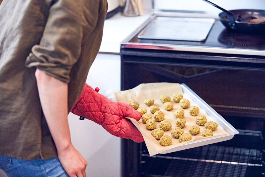 A woman holds a tray of uncooked falafel, ready to place them in the oven for cooking. Making dinner for the week.