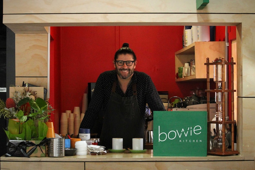 A man stands behind a coffee stand inside a cafe