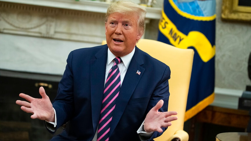 President Donald Trump speaks with his hands outstretched while sitting in a yellow chair.