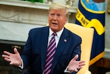 President Donald Trump speaks with his hands outstretched while sitting in a yellow chair.