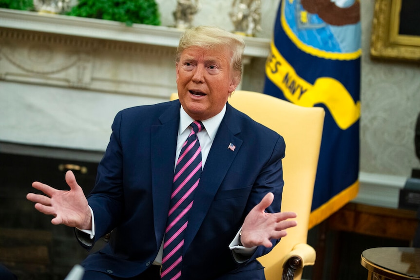 President Donald Trump speaks with his hands outstretched while sitting in a yellow chair.