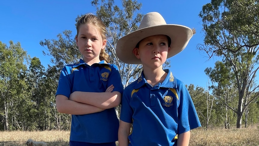 Two kids stand in a field looking unimpressed 