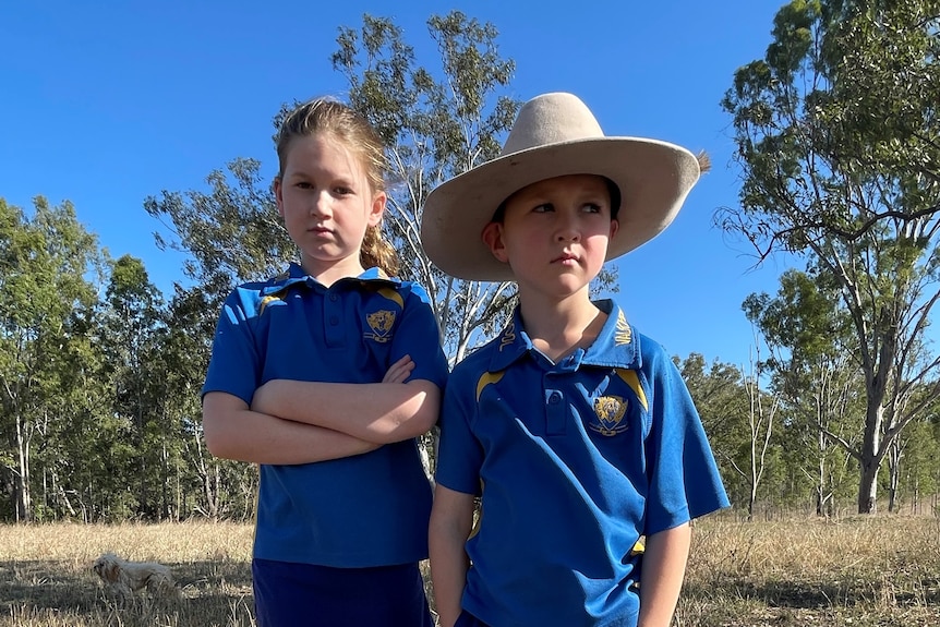 Two kids stand in a field looking unimpressed 