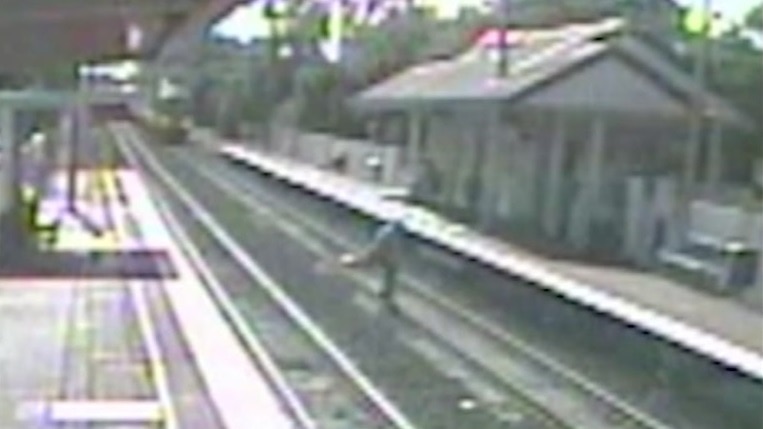 Man crossing rail line as train approaches.