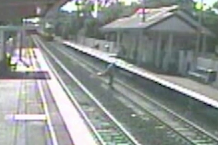 Man crossing rail line as train approaches.