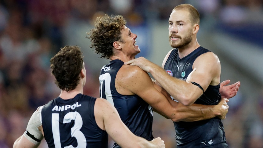 A Carlton AFL player is surrounded by teammates after he kicks a vital goal.