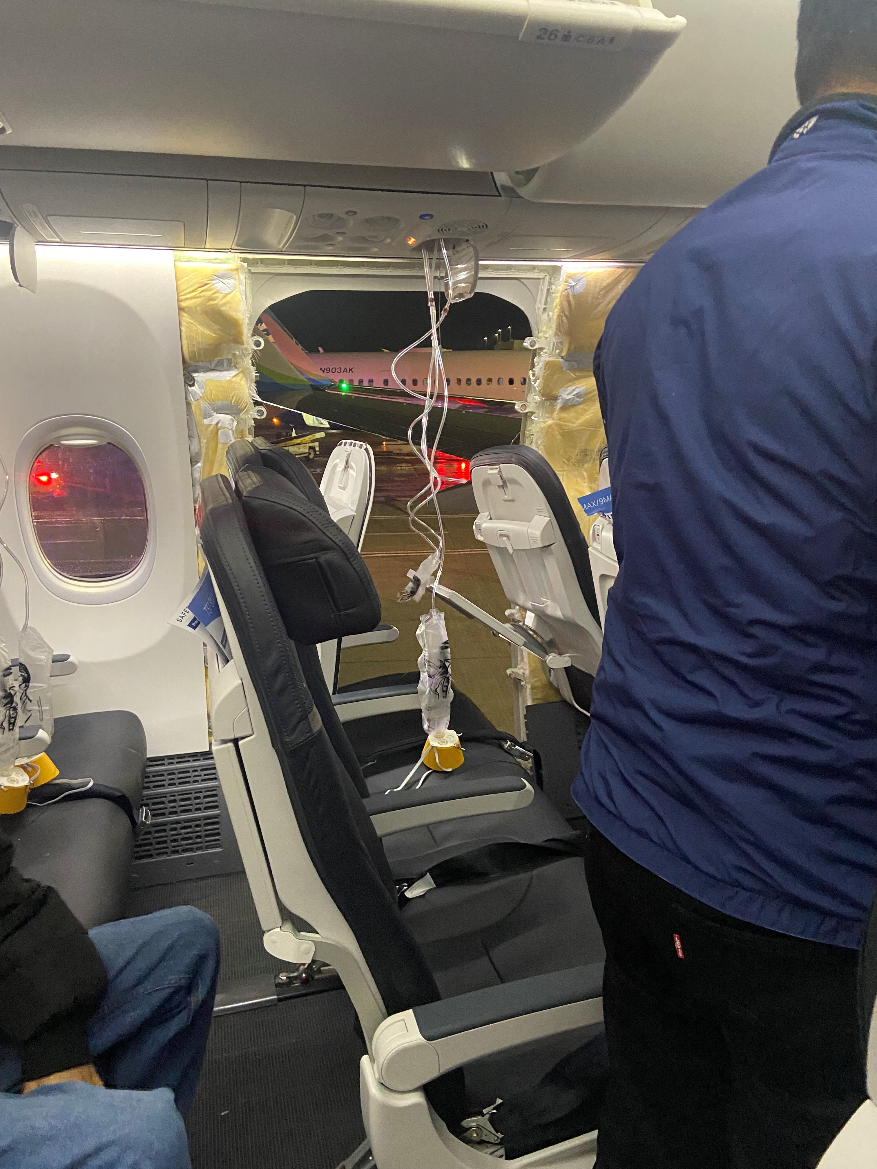 Oxygen masks dangle in front of several plane seats with the window missing from a plane.