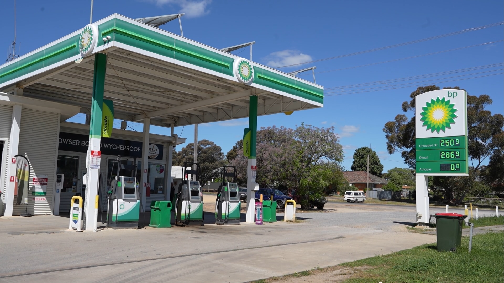 Green and white BP service station in Wycheproof, sun shining on the pumps, tall roof and tree next to station
