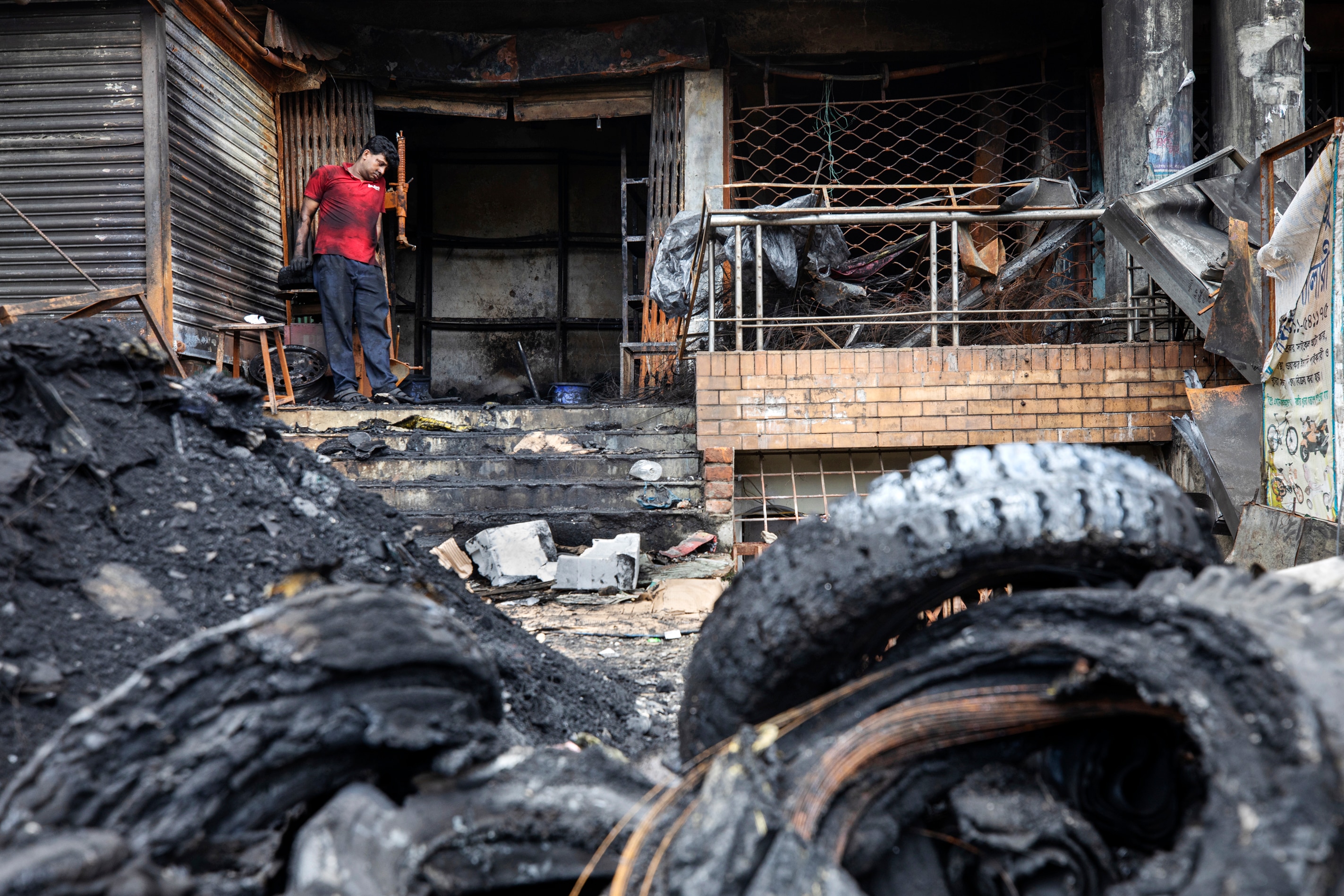 A man inspects burnt tyres in front of his shop which was torched during riots