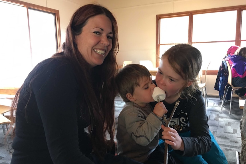 A mother and her two children eat a marshmallow.