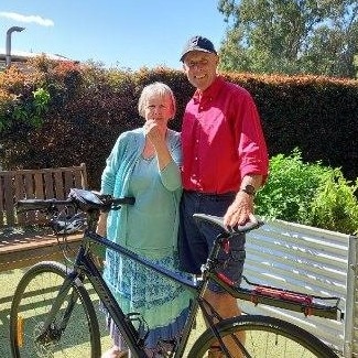 An elderly woman in green dress and man in red shirt standing next to a pushbike.