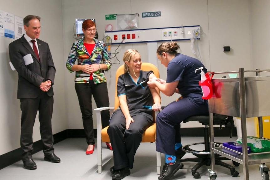 a woman receiving a needle jab while two people look on