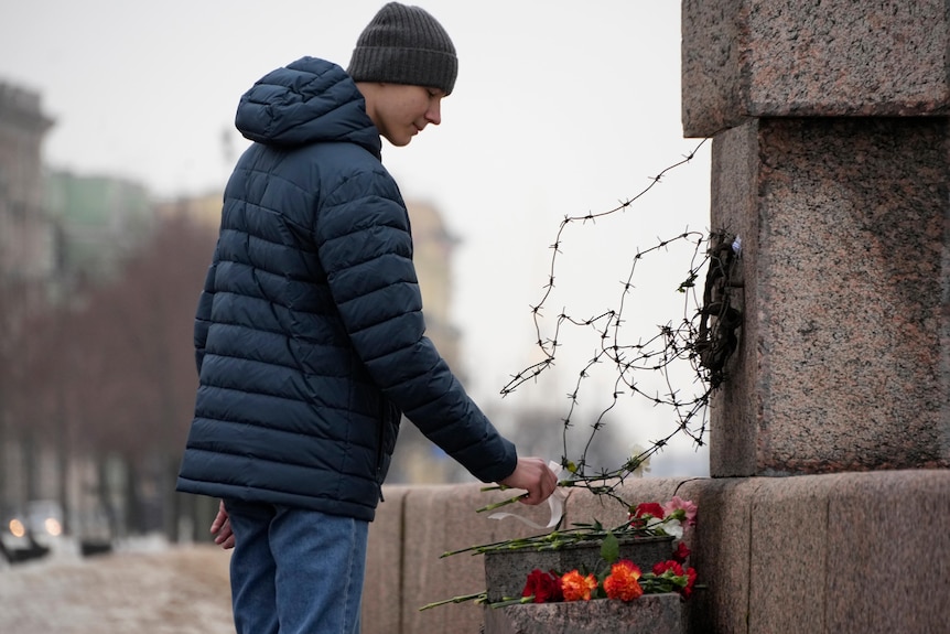 A man leaves a flower at an outdoor shrine which has barbed wire on it