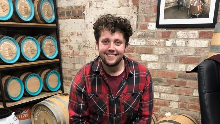 A man looks at the camera while sitting on whiskey barrel.
