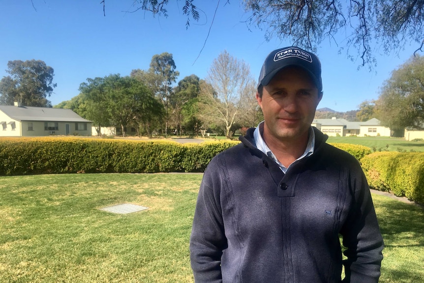 Adam White stands with hands in pocket in front of a street with houses and trees behind him