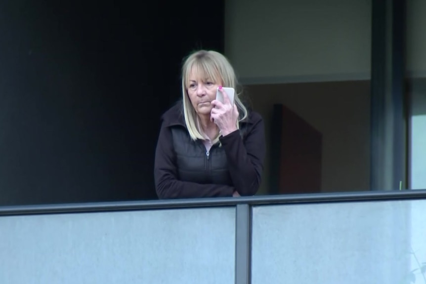 Une femme écoute son téléphone sur un balcon.