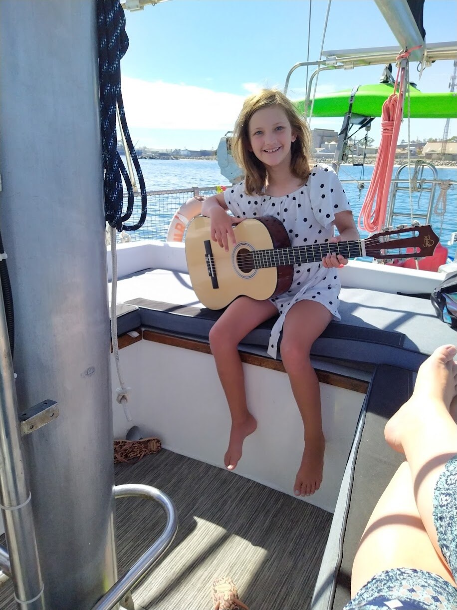 Young girl practices her guitar on board a sailing boat.