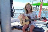 Young girl practices her guitar on board a sailing boat.