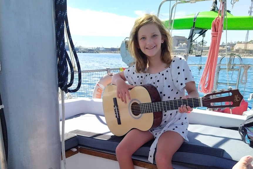 Young girl practices her guitar on board a sailing boat.