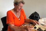 Dawn Fletcher flicks through old photos of her time in the Australian Navy. She is wearing an orange top and wide smile.