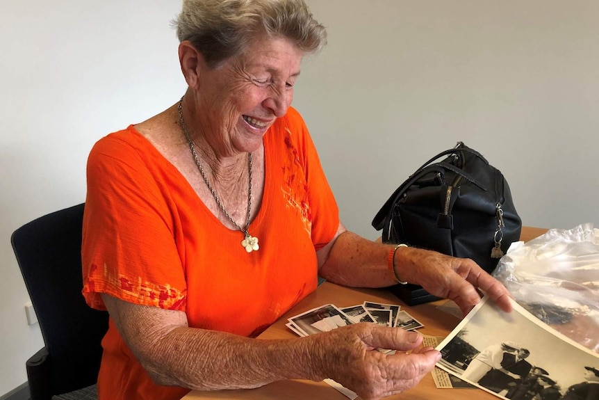 Dawn Fletcher flicks through old photos of her time in the Australian Navy. She is wearing an orange top and wide smile.