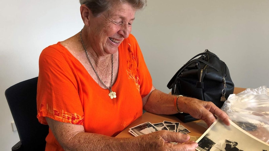 Dawn Fletcher flicks through old photos of her time in the Australian Navy. She is wearing an orange top and wide smile.