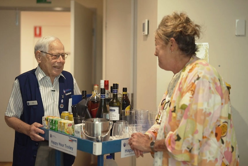 Colin Apelt stands next to a trolley laden with alcoholic and non-alcoholic drinks and talks to a woman