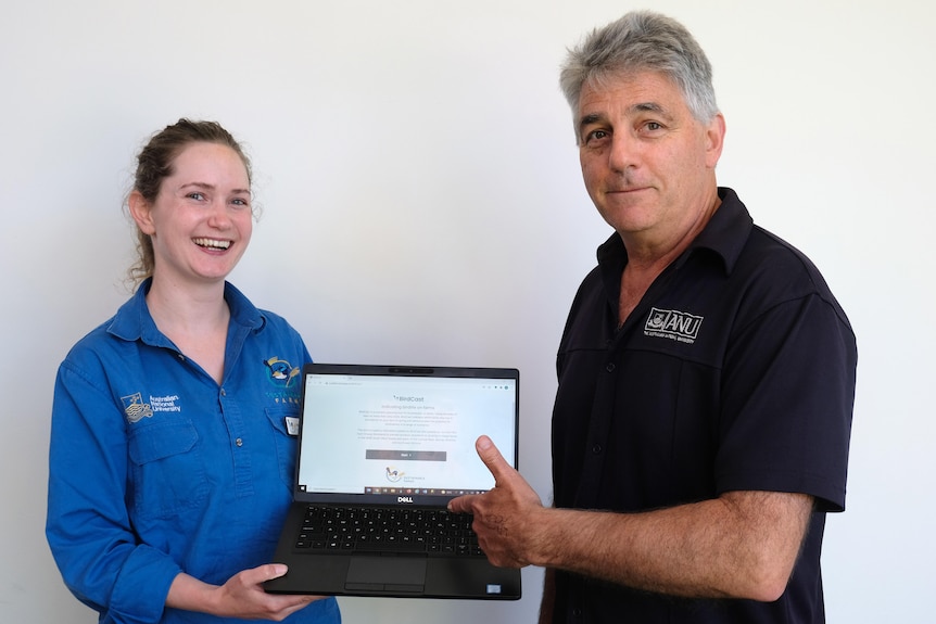 A woman and man stand with a computer between them.