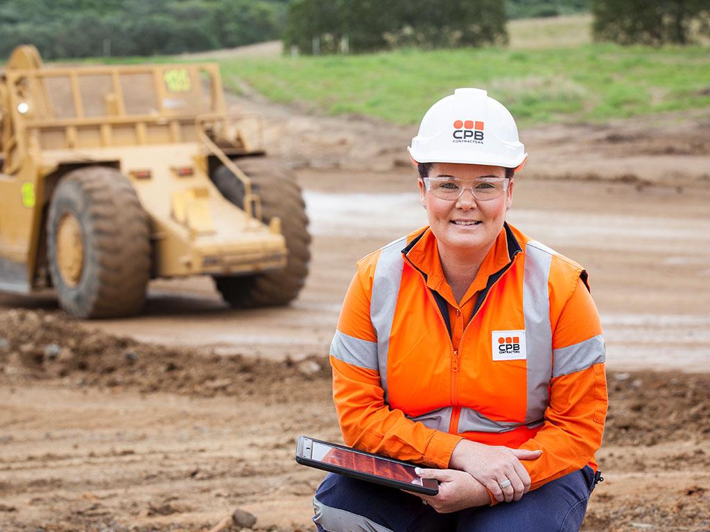 A woman in high-vis and a construction hard hat on a dirt construction site.