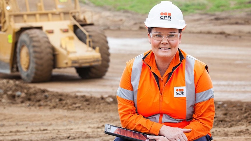 A woman in high-vis and a construction hard hat on a dirt construction site.